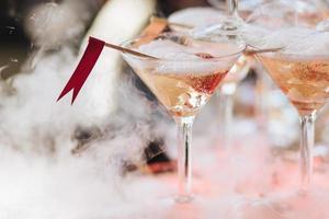 Smoke pours out of glass with sparkling fizz beverage. Alcoholic drink or cocktail in glass with ice and white fog. Club drinks for special occasions. Spalsh of wine with smoke photo