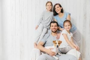 retrato de familia feliz interior. un padre guapo sostiene un perro, una hermosa madre morena y dos hijas, se divierten juntos, posan para el álbum familiar, pasan tiempo juntos. personas, concepto de relaciones foto