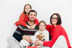 retrato de familiares felices con expresiones positivas, abrazarse y apoyarse mutuamente, tener una buena relación. padre encantado, madre, dos hermanas y un pequeño cachorro posan juntos en el interior. foto