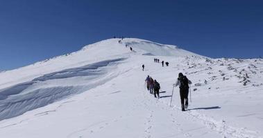 Wanderer, die an einem sonnigen Wintertag in der Schlange zum Gipfel laufen. schneebedeckter Berg. Expedition zum Gipfel. Verbindung mit der Natur. Winterreisen. Gedenkspaziergang.