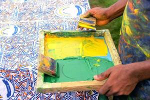 Hand an artist pressing squeegee on a screen printing box to print on cloth photo