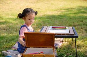 A little girl is sitting on the cloth and painted on the paper placed on a table photo