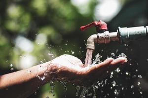 concepto de agua en la vida cotidiana. manos sosteniendo el agua que fluye del grifo. agua salpicando del grifo foto