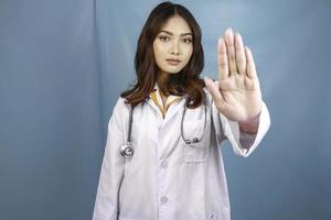 Serious Asian female doctor with stethoscope and white coat, showing stop sign. photo