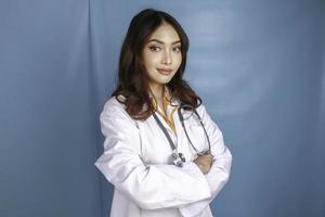 Portrait of an attractive confident female doctor, friendly smiling arms crossed wear white lab coat stethoscope isolated blue color background photo