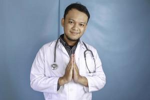 un joven médico asiático está sonriendo y dando un gesto de saludo foto