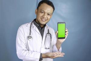 Young Asian man doctor is showing green screen or copy space on his smartphone photo