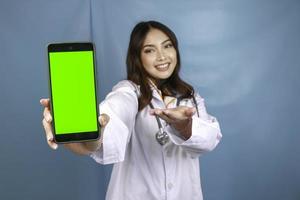 una joven doctora asiática sonríe y muestra una pantalla verde o copia espacio en su teléfono inteligente foto