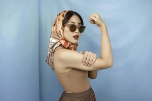 Retro concept of a young Asian strong woman showing her biceps isolated by a blue background photo