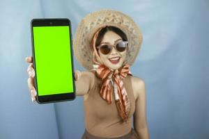 concepto de viaje de una joven mujer feliz asiática que muestra espacio de copia en su teléfono inteligente aislado por un fondo azul foto