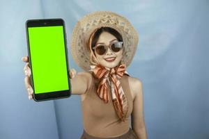 Traveling concept of a young Asian happy woman showing copy space on her smartphone isolated by a blue background photo