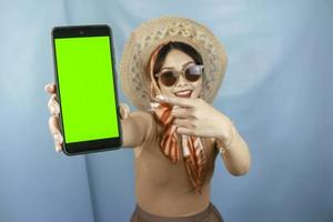 concepto de viaje de una joven mujer feliz asiática que muestra espacio de copia en su teléfono inteligente aislado por un fondo azul foto