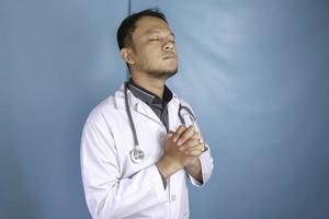 A portrait of a young Asian male doctor is praying to God photo