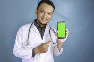 un joven médico asiático muestra una pantalla verde o copia espacio en su teléfono inteligente foto