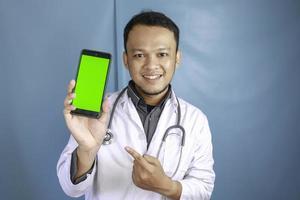 Young Asian man doctor is showing green screen or copy space on his smartphone photo