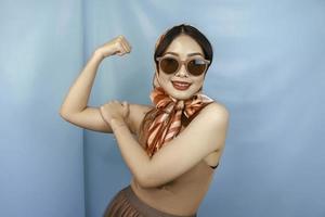 concepto retro de una joven mujer fuerte asiática que muestra sus bíceps aislados por un fondo azul foto