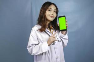 Young Asian woman doctor is pointing and showing green screen or copy space on her smartphone photo
