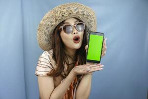 joven mujer feliz asiática mostrando e impactando a su teléfono inteligente aislado por un fondo azul foto