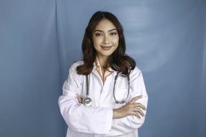 Portrait of an attractive confident female doctor, friendly smiling arms crossed wear white lab coat stethoscope isolated blue color background photo