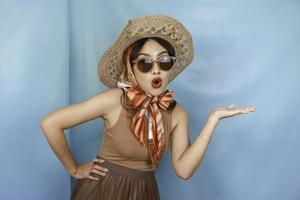 Young Asian shocked woman isolated by a blue background pointing copy space on the side. photo