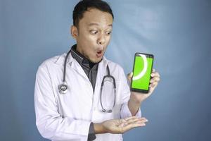 Young Asian man doctor is showing green screen or copy space on his smartphone photo