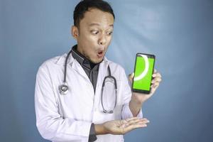 Young Asian man doctor is showing green screen or copy space on his smartphone photo