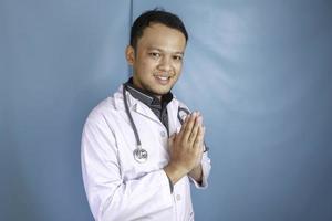 A young Asian male doctor is smiling and giving greeting gesture photo
