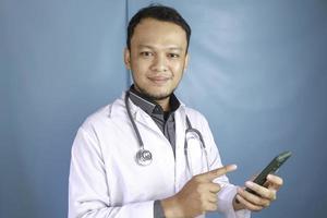 Young Asian man doctor is smiling and pointing his smartphone photo
