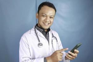 Young Asian man doctor is smiling and pointing his smartphone photo