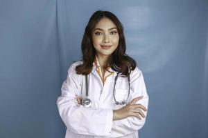 Portrait of an attractive confident female doctor, friendly smiling arms crossed wear white lab coat stethoscope isolated blue color background photo