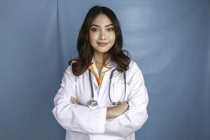 retrato de una doctora atractiva y segura de sí misma, brazos sonrientes amistosos cruzados usar bata de laboratorio blanca estetoscopio aislado fondo de color azul foto