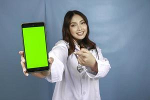 Young Asian woman doctor is smiling and showing green screen or copy space on her smartphone photo