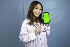 Young Asian woman doctor is pointing and showing green screen or copy space on her smartphone photo