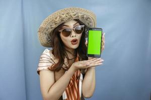 Young Asian happy woman showing and shocking to her smartphone isolated by a blue background photo