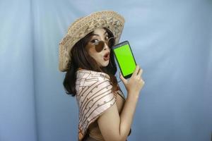 Young Asian happy woman showing green screen on her smartphone isolated by a blue background photo