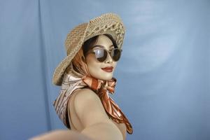 Traveling concept of a young Asian woman taking a selfie isolated by a blue background photo