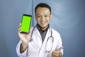 un joven médico asiático muestra una pantalla verde o copia espacio en su teléfono inteligente foto