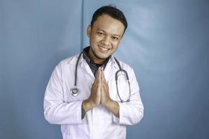 A young Asian male doctor is smiling and giving greeting gesture photo