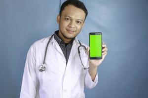 Young Asian man doctor is showing green screen or copy space on his smartphone photo