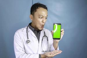 Young Asian man doctor is showing green screen or copy space on his smartphone photo