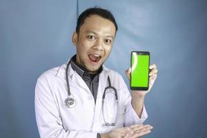 un joven médico asiático muestra una pantalla verde o copia espacio en su teléfono inteligente foto