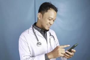 Young Asian man doctor is smiling and pointing his smartphone photo