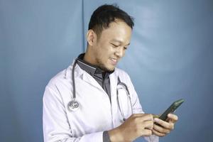 el joven médico asiático está sonriendo y señalando su teléfono inteligente foto