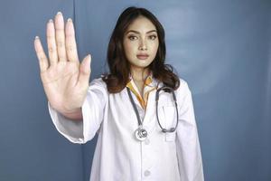 Serious Asian female doctor with stethoscope and white coat, showing stop sign. photo