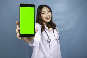 una joven doctora asiática sonríe y muestra una pantalla verde o copia espacio en su teléfono inteligente foto