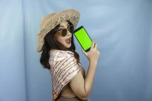 Young Asian happy woman showing green screen on her smartphone isolated by a blue background photo