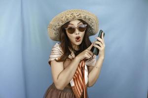 Young Asian woman pointing and shocking to her smartphone isolated by a blue background photo