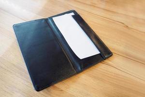 Blank empty white paper in black leather restaurant payment billing receipt folder on wood table photo