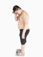 Soft focus of fat boy disappoint his fatness while standing on on weighing machine over white background photo