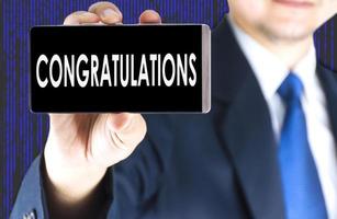 Focused of congratulations word on mobile phone screen in blurred young businessman hand and digital technology background photo